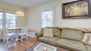 A living room with a wooden dining table, white chairs, a green sofa, and a painting of palm trees. - Walk to Beach & Boardwalk: Jersey Shore Cottage! (North Wildwood)