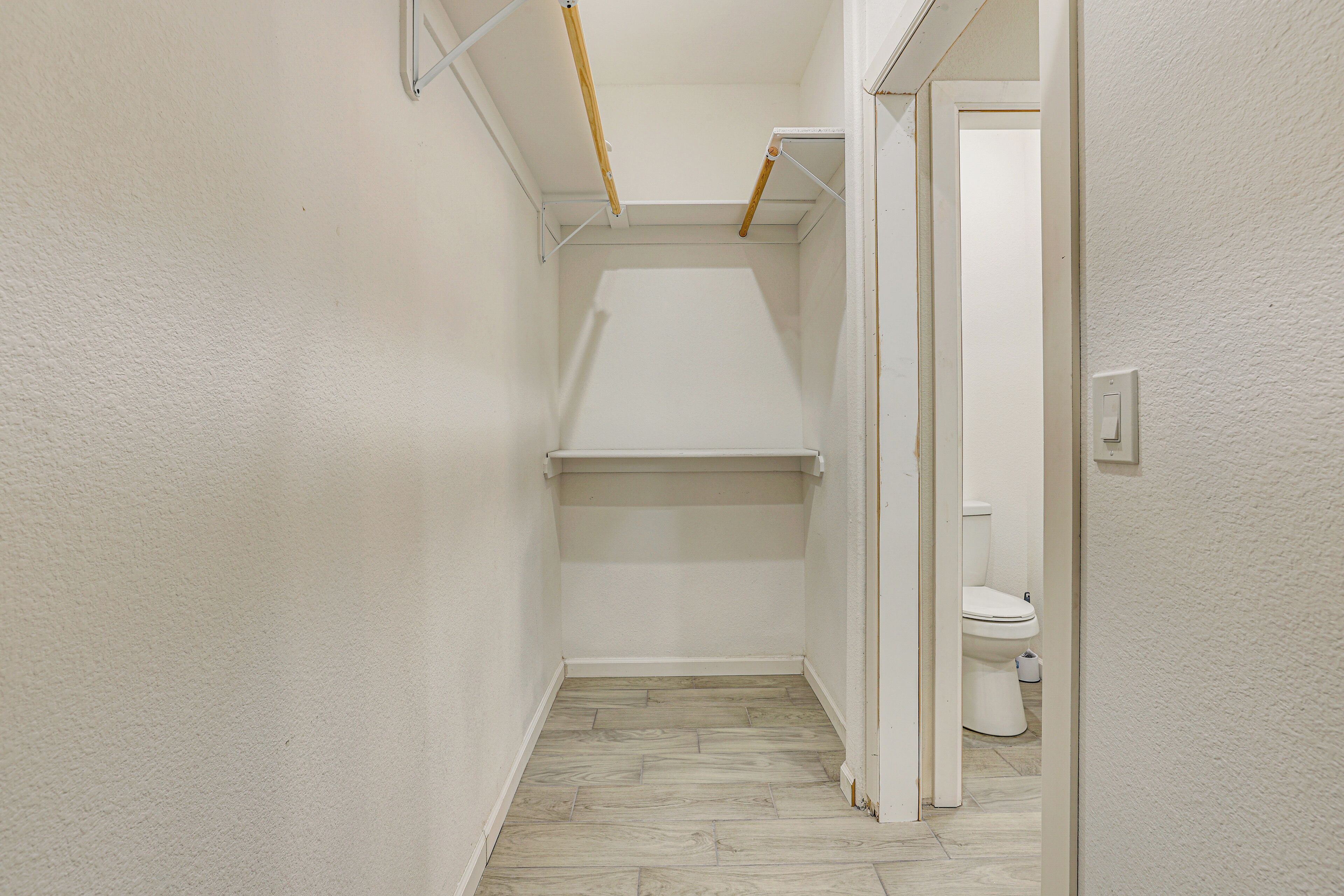 A narrow hallway with a toilet and a shelf unit.