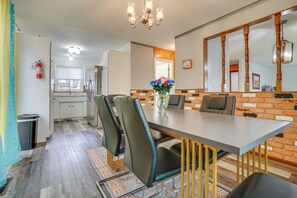 Un espace repas avec une longue table, des chaises et un vase rempli de fleurs. On y trouve un mur en briques et un plafond avec une poutre en bois.