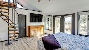 A bedroom with a wooden staircase, a bed with a patterned bedspread, a dresser, and a television on the wall.