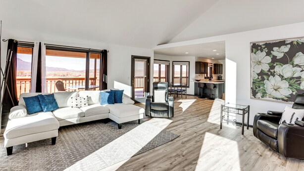 A spacious living room with a white sectional sofa, a leather armchair, and a dining area with a view of the mountains.