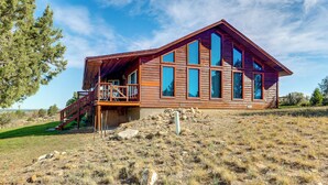 A wooden cabin with a balcony and large windows, situated on a grassy hill. - Mtn-view Escape w/ Office Space in Cortez! (Cortez)