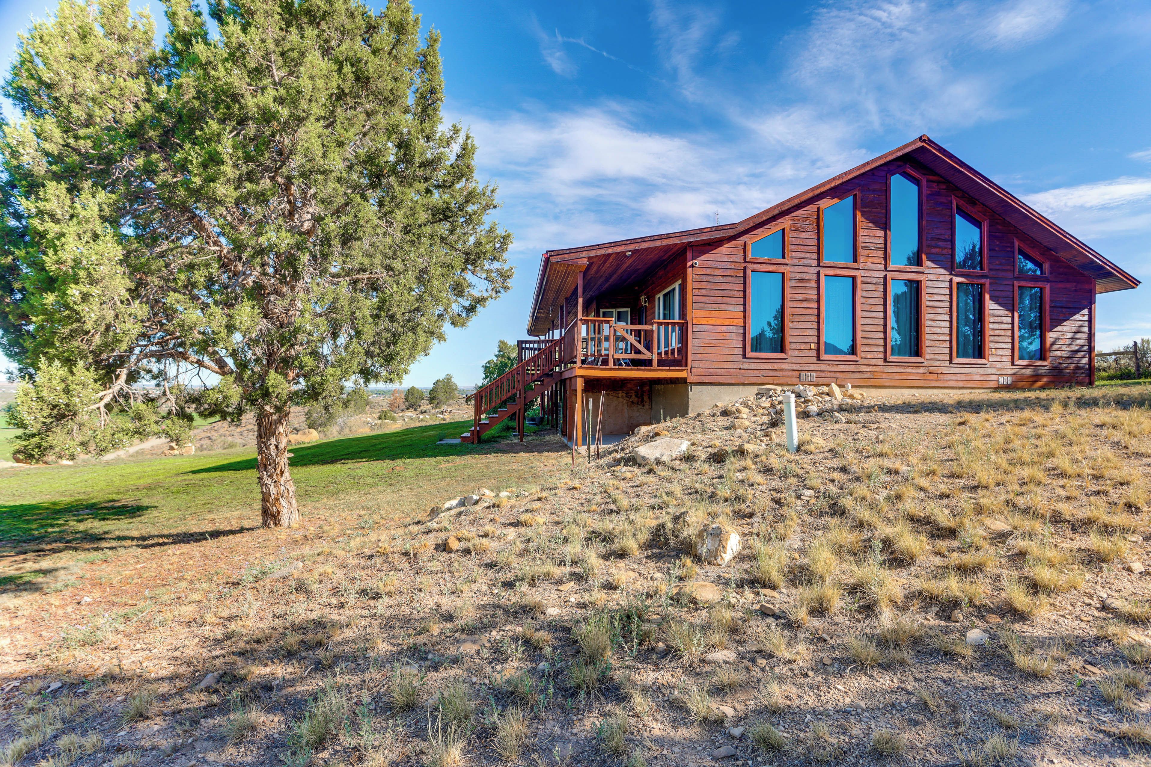 A wooden cabin with a balcony, surrounded by a grassy landscape and a large tree.