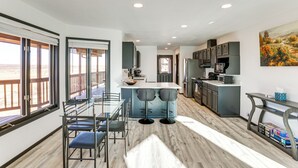 A modern kitchen with a central island, bar stools, and a dining area with a glass table and chairs.