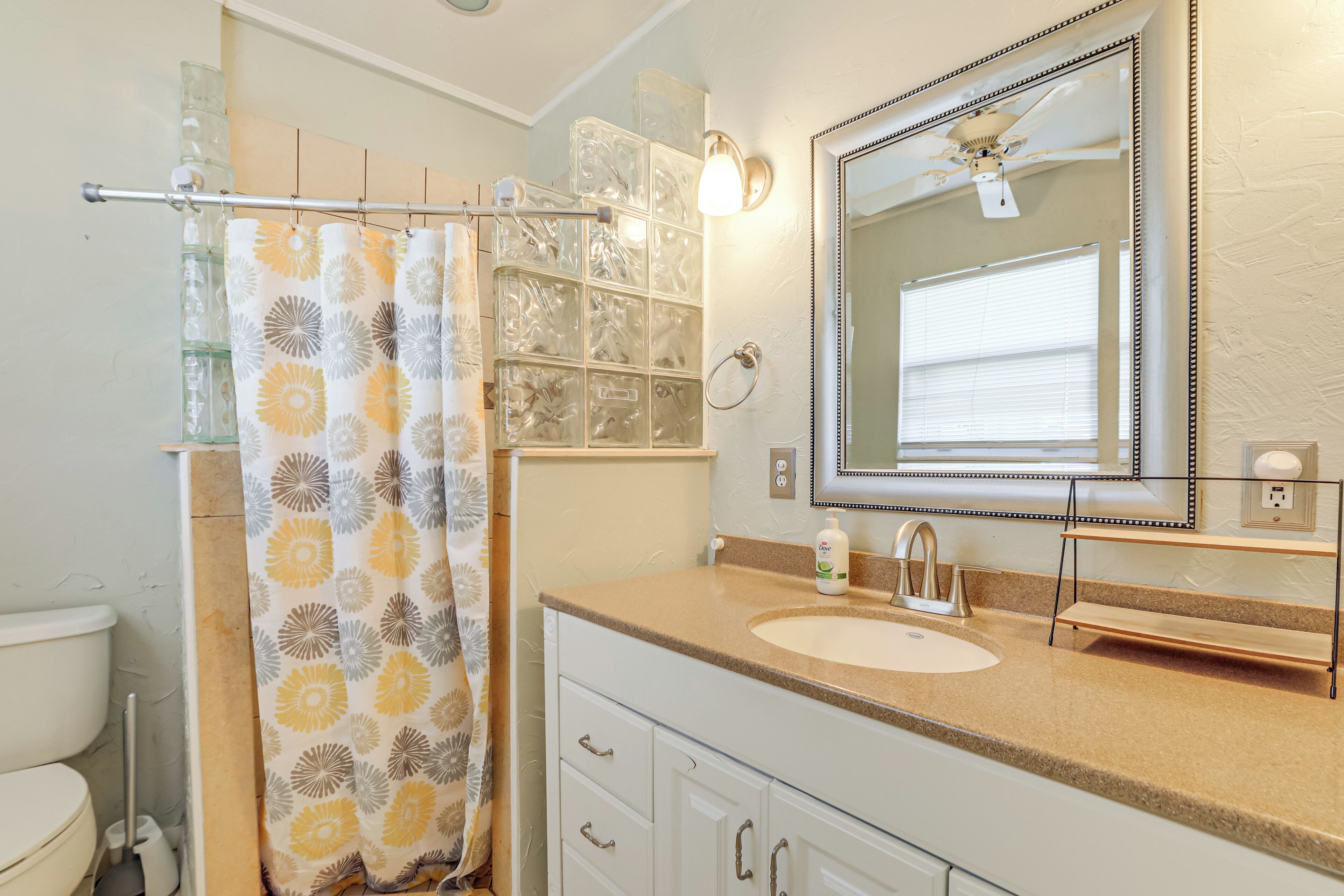 A bathroom with a toilet, a shower curtain, a sink, a mirror, and a ceiling fan.