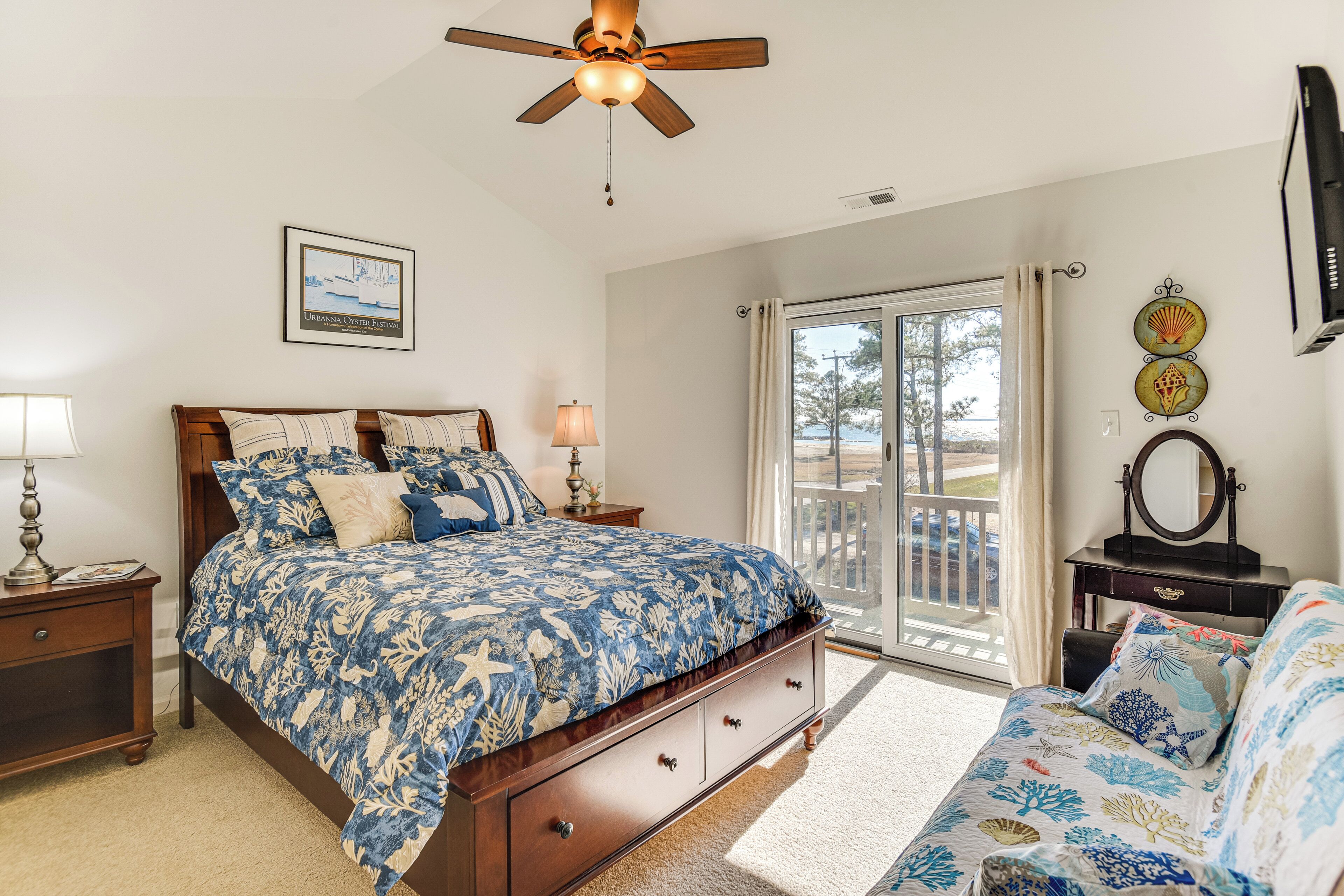 A bedroom with a bed, a nightstand, a dresser, a ceiling fan, a window with curtains, and a balcony.