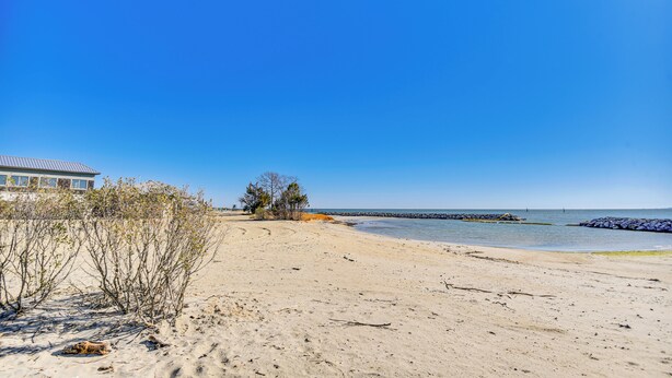 Ein Strand mit blauem Himmel, sandigem Ufer und einem Gebäude im Hintergrund.