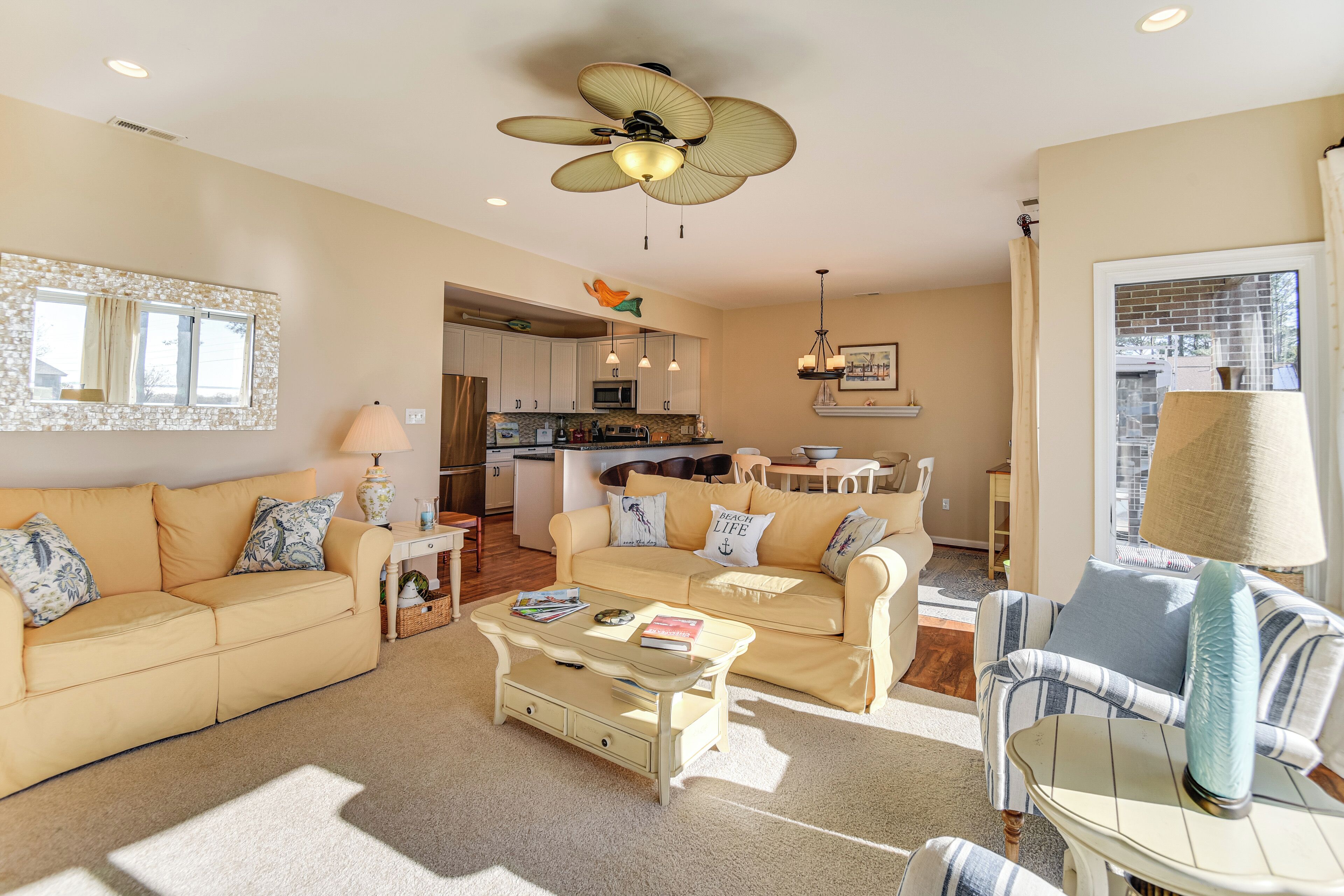 A spacious living room with a beige sofa, a coffee table, and a striped armchair.