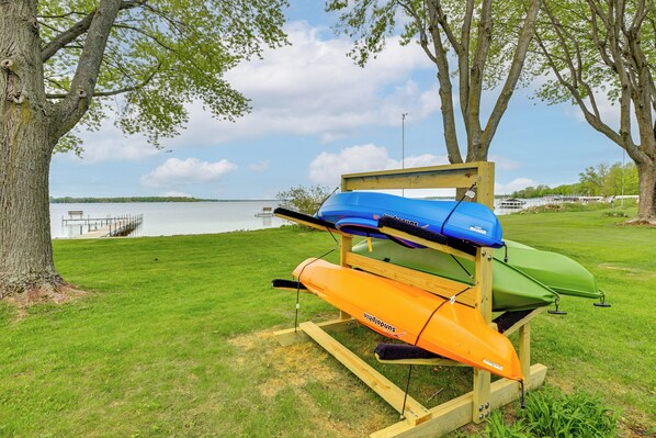 A kayak rack with three kayaks in a grassy area near a body of water.