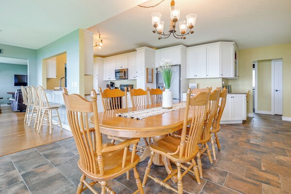 A spacious dining area with a large wooden table and chairs, a chandelier, and a kitchen in the background. - Shawano Lake House w/ Boat Dock, Kayaks, & Grill! (Cecil)