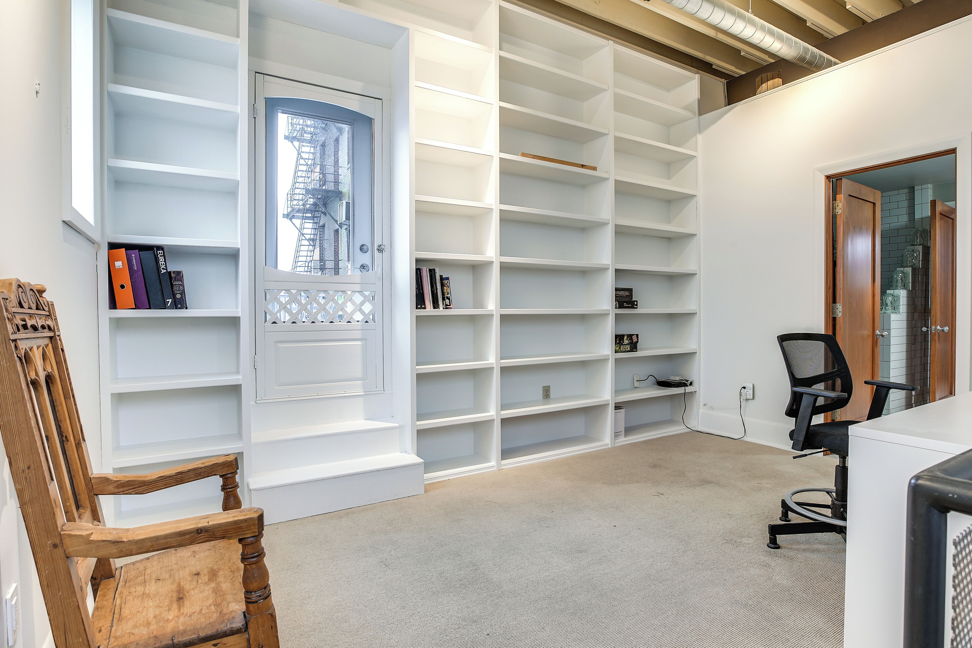 A room with a large white shelving unit, a wooden chair, and a desk with a computer.