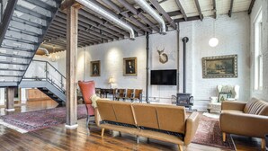 A spacious living area with a wooden floor, a staircase, a sofa, a chair, and a television. - < 1 Mi to Wittenberg: Eclectic Loft w/ Parking! (Springfield)