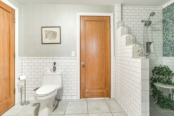 A bathroom with a toilet, a wooden door, a shower with a glass enclosure, and a small plant on a metal stand. - < 1 Mi to Wittenberg: Eclectic Loft w/ Parking! (Springfield)