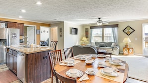 A dining area with a wooden table set for four, a kitchen with a refrigerator, and a living room with a sofa and a lamp. - Mountain View Retreat Relax & Unwind (Midway)