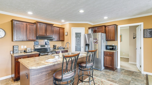 A modern kitchen with wooden cabinets, a stainless steel refrigerator, and a central island with bar stools. - Mountain View Retreat Relax & Unwind (Midway)