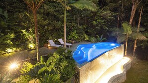 Una piscina rodeada de exuberante vegetación, con sillas de descanso y un solárium pavimentado.