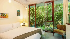 Un dormitorio con cama, una silla y un ventanal con vistas a follaje.