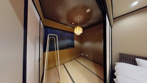 Una habitación con suelo de tatami, una lámpara colgante, una escalera y una cama con ropa blanca.