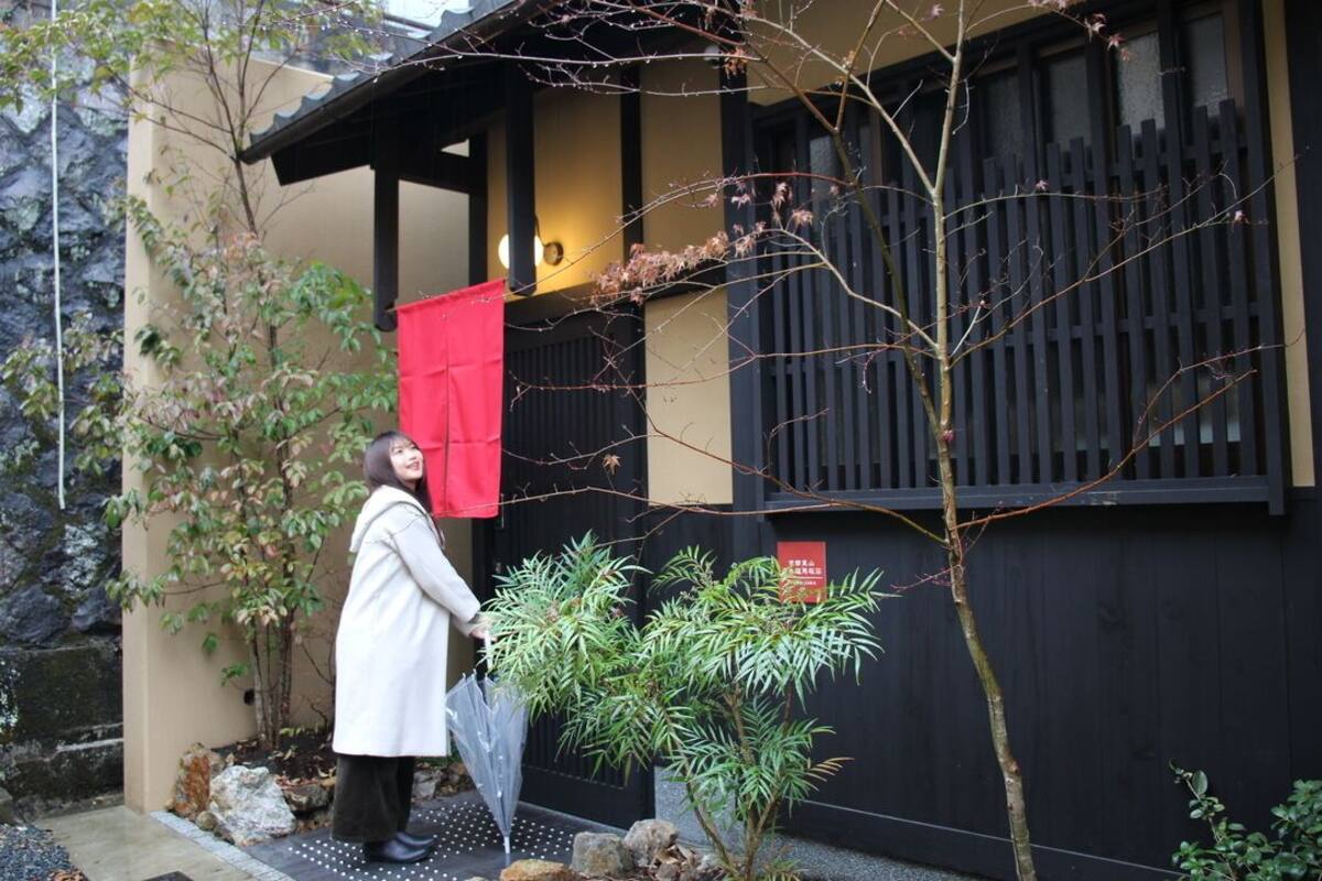 A person standing in front of a building with a black exterior and a red cloth hanging on the door.