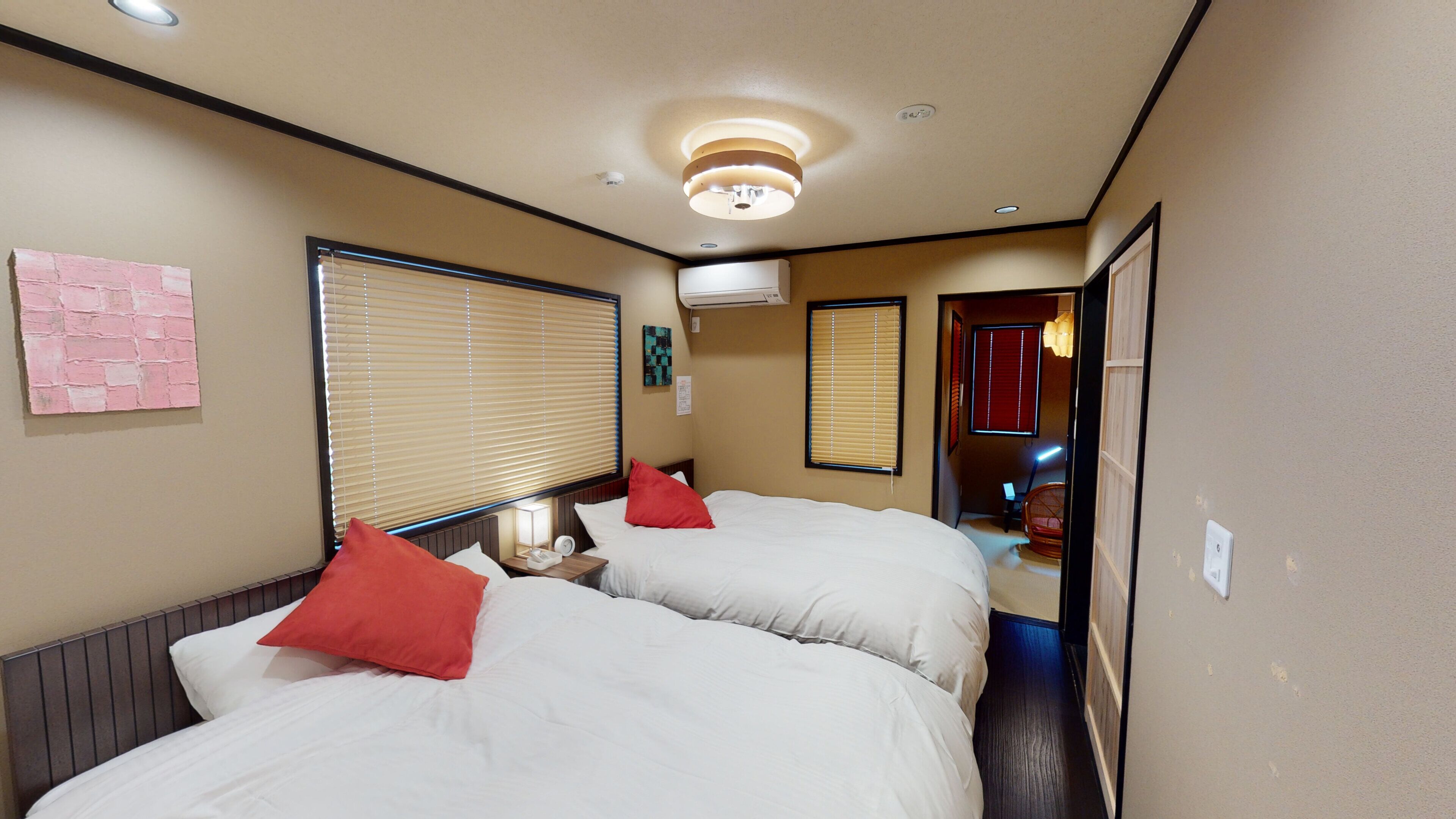 Hotelkamer met twee bedden, een wandairconditioner, een nachtkastje met lamp en een raam met zonwering.