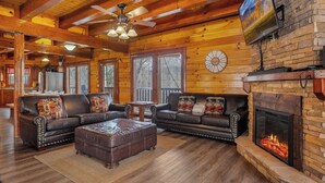 A spacious living room with wooden floors, leather sofas, a fireplace, and a ceiling fan. - Private Indoor Pool, Hot Tub, Fire Pit, Pool Table, Free Attractions! (Cosby)