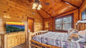 A wooden cabin interior with a bed, a dresser, a ceiling fan, and a large window. - Private Indoor Pool, Hot Tub, Fire Pit, Pool Table, Free Attractions! (Cosby)