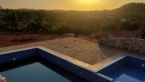 A rectangular swimming pool with a tiled edge, surrounded by a brick pathway, and a view of the landscape in the background. - Pito Guest House (Elmina)
