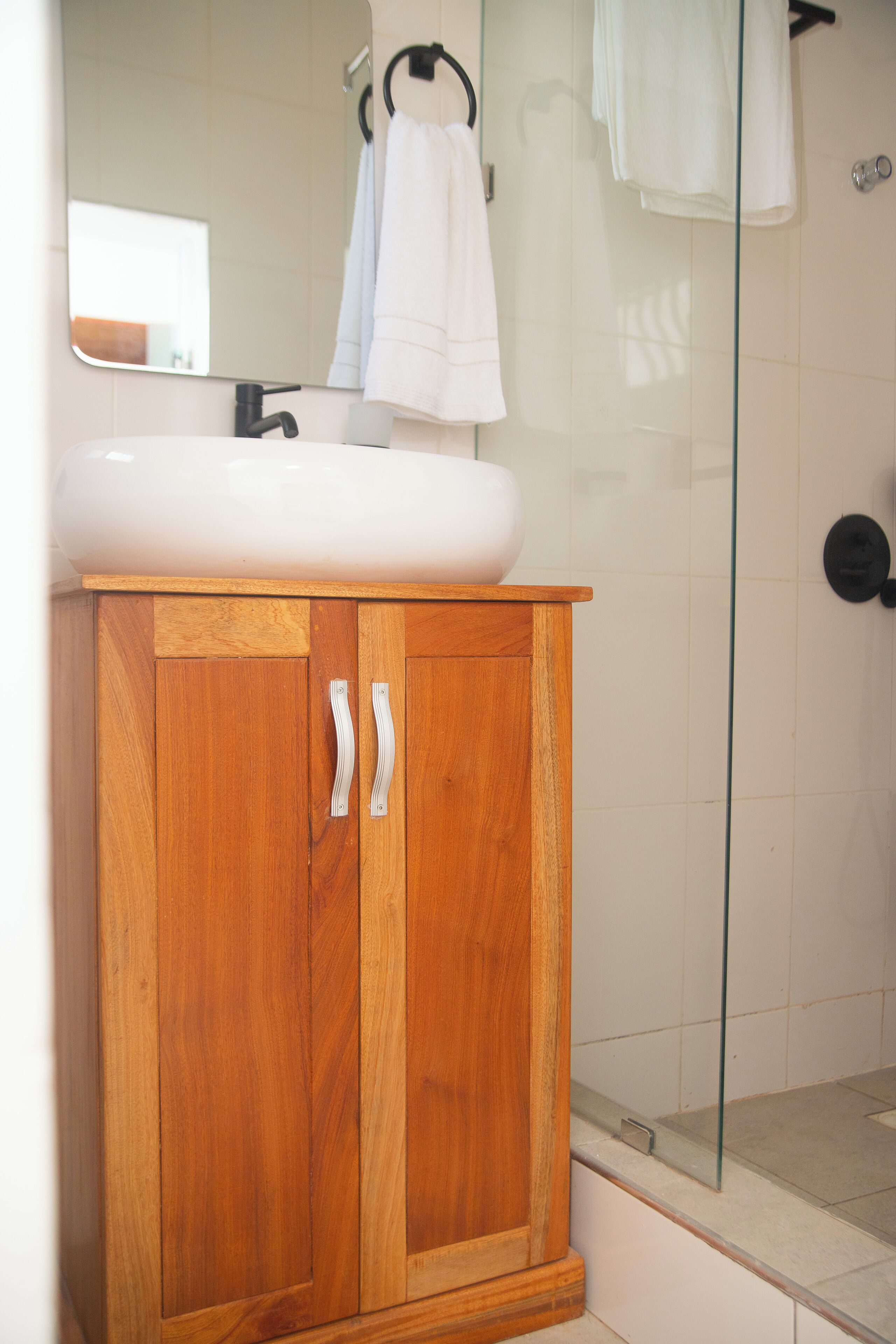 A wooden cabinet with a white sink, a glass shower enclosure, and a mirror above the sink.