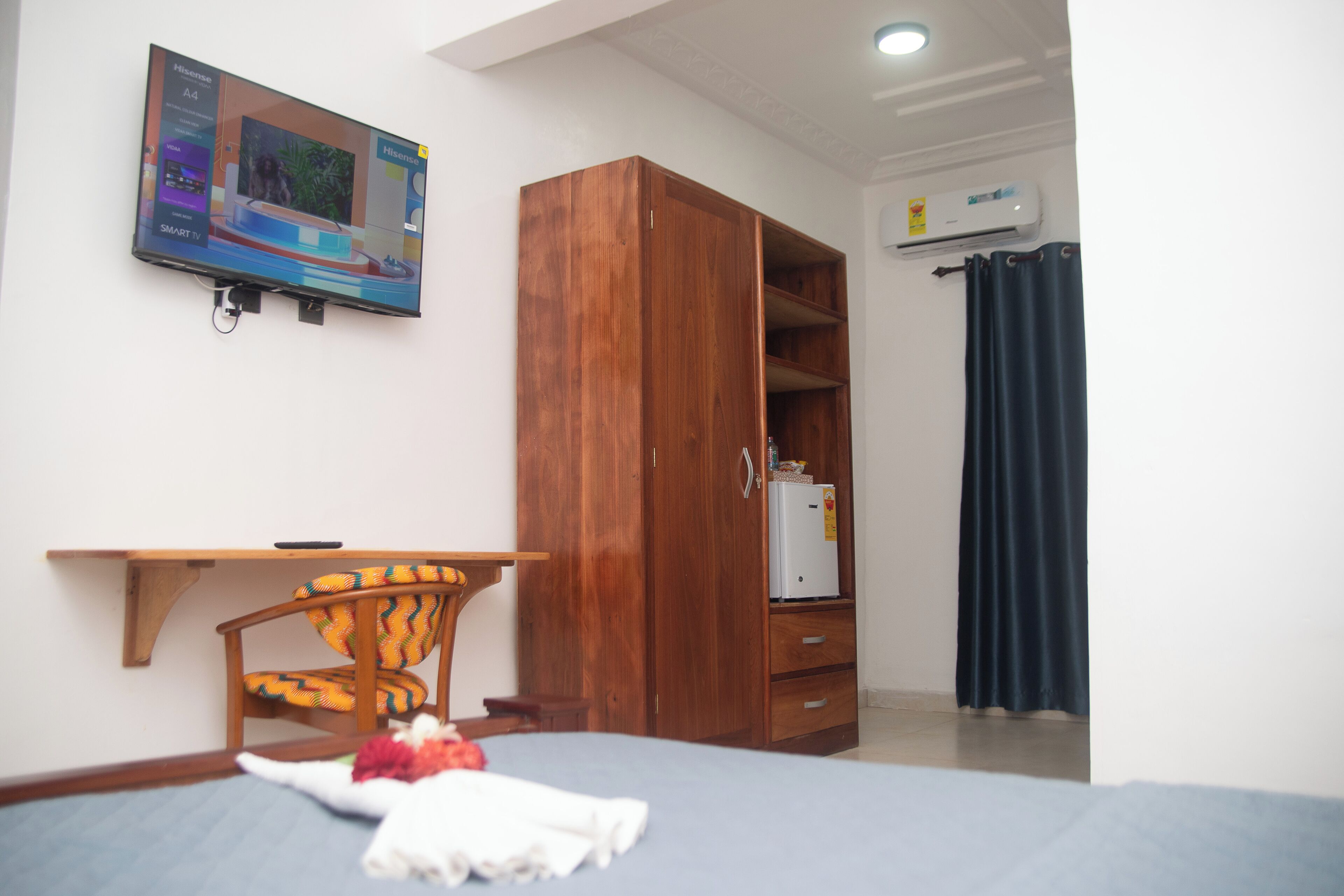 Un dormitorio con cama, armario de madera, escritorio, silla y televisor montado en la pared.