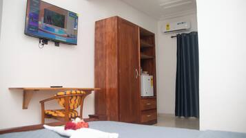 Un dormitorio con cama, armario de madera, escritorio, silla y televisor montado en la pared.
