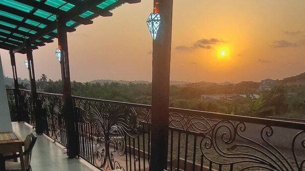 An outdoor seating area with tables and chairs, a coffee machine, and a view of the sunset. - Pito Guest House (Elmina)