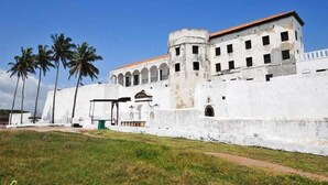 A large, white fortress-like building with multiple arched windows and a central tower. - Pito Guest House (Elmina)