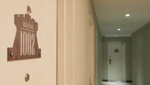 Een gang met een bordje waarop 'KAMER 1002' staat.