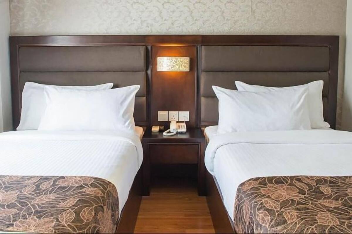 Habitación de hotel con dos camas, una mesita de noche entre ellas y una lámpara fijada a la pared.