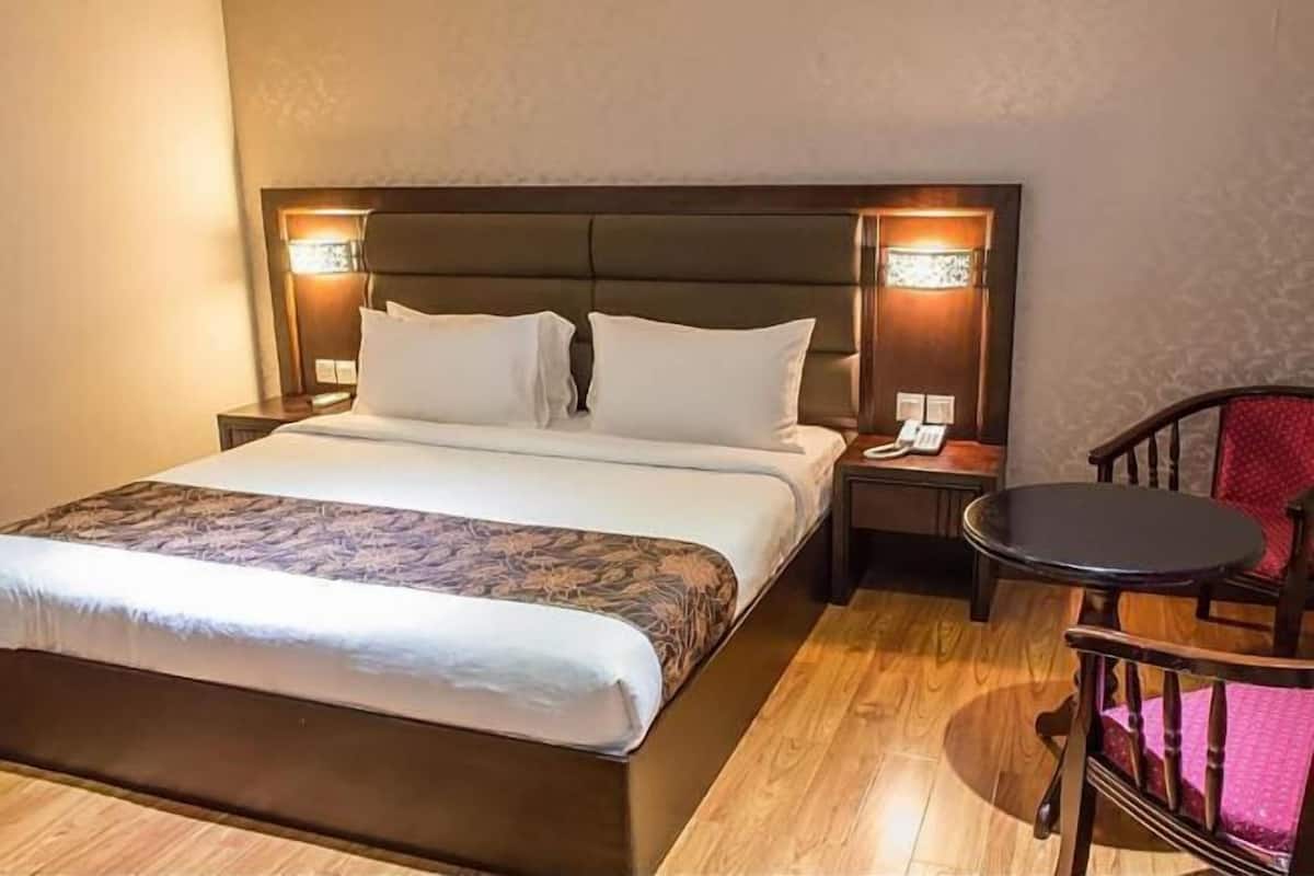 Habitación de hotel con una cama grande, una mesita de noche con lámpara y una pequeña mesa redonda con una silla.