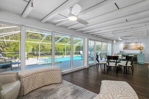 A spacious living area with large windows, a ceiling fan, and a view of a swimming pool.