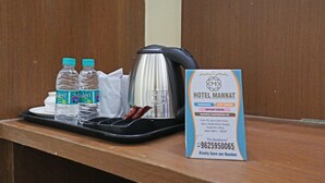 Zona de recepción de un hotel con una bandeja que contiene dos botellas de agua, una tetera y una taza blanca. Se ve un cartel con el nombre del hotel y sus servicios.