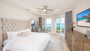 A spacious bedroom with a large bed, a ceiling fan, a TV, and a view of the ocean through the sliding glass doors. - Seabreeze 8 - Luxury 4-bedroom on Seven Mile Beach (Seven Mile Beach)