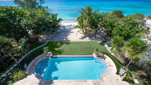 A pool with a view of the ocean, surrounded by palm trees and a well-maintained lawn. - Seabreeze 8 - Luxury 4-bedroom on Seven Mile Beach (Seven Mile Beach)