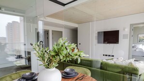 Un comedor moderno con una mesa de madera, cuencos negros y un florero blanco con follaje verde.