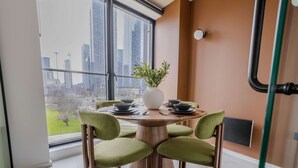 Un comedor con una mesa redonda de madera, cuatro sillas verdes y un jarrón blanco con una planta.