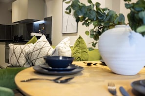 A dining area with a round table, a bowl, cutlery, and green cushions. - Verdana Suite 1BD Flat Near Centre (Manchester)