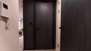 Un corridoio con una porta in legno scuro, un citofono a parete e un pavimento piastrellato.