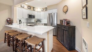 A kitchen with white cabinets, a stainless steel refrigerator, a large island with stools, and a dark wooden cabinet.