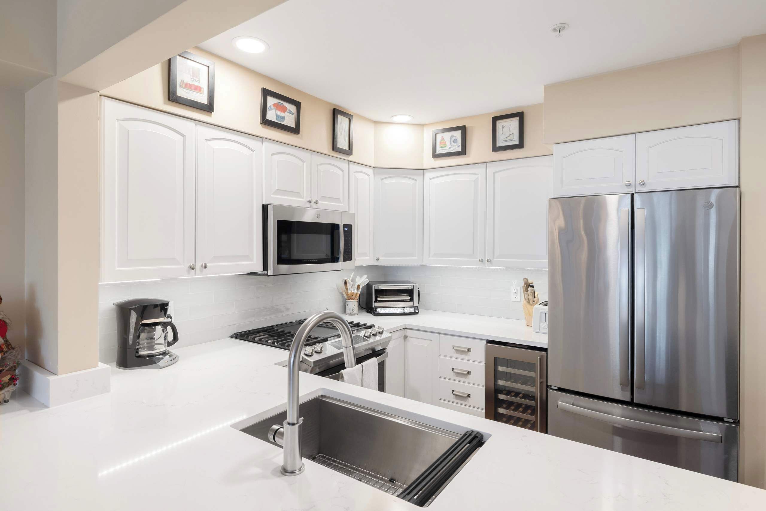 A modern kitchen with white cabinets, stainless steel appliances, a sink, and a coffee maker.