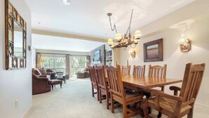 A dining area with a wooden table and chairs, a chandelier, and a TV mounted on the wall.