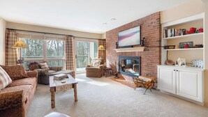 A cozy living room with a fireplace, a sofa, a coffee table, and a bookshelf.