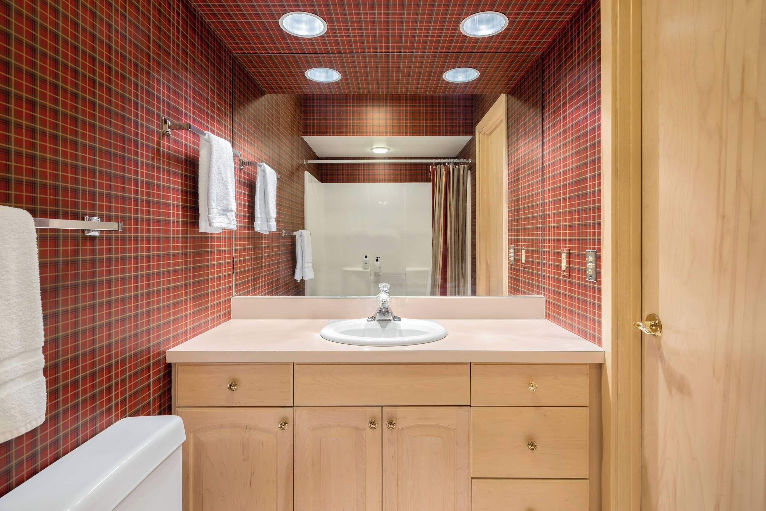 A bathroom with a red and black checkered wall, a white sink, and wooden cabinets.