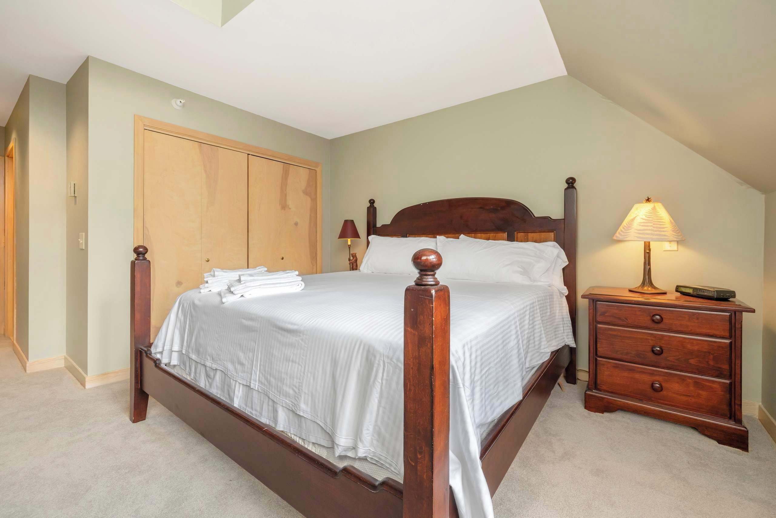 A bedroom with a wooden four-poster bed, a nightstand with a lamp, and a closet.