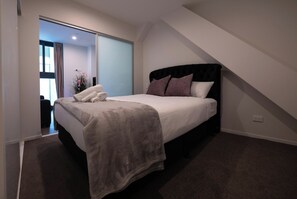 A bedroom with a bed, a large window, and a view of the outside.